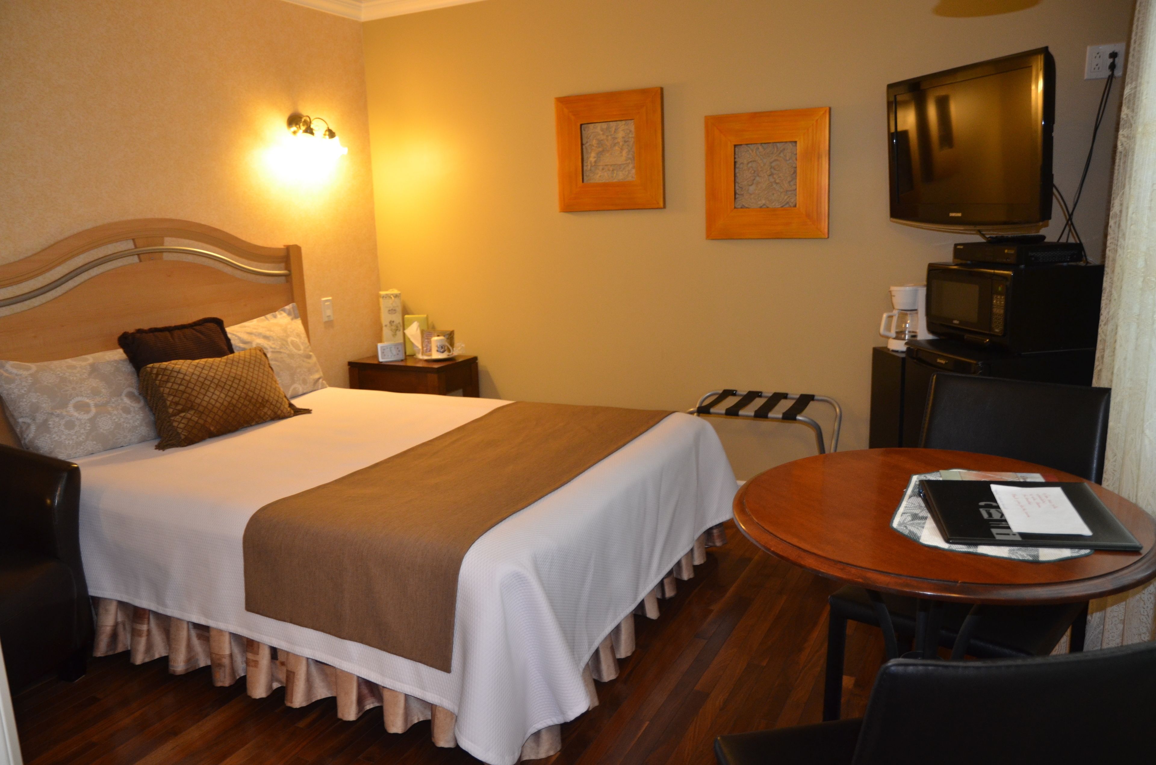 A hotel room with a bed, bedside table, lamp, television, and a small round table with a chair.