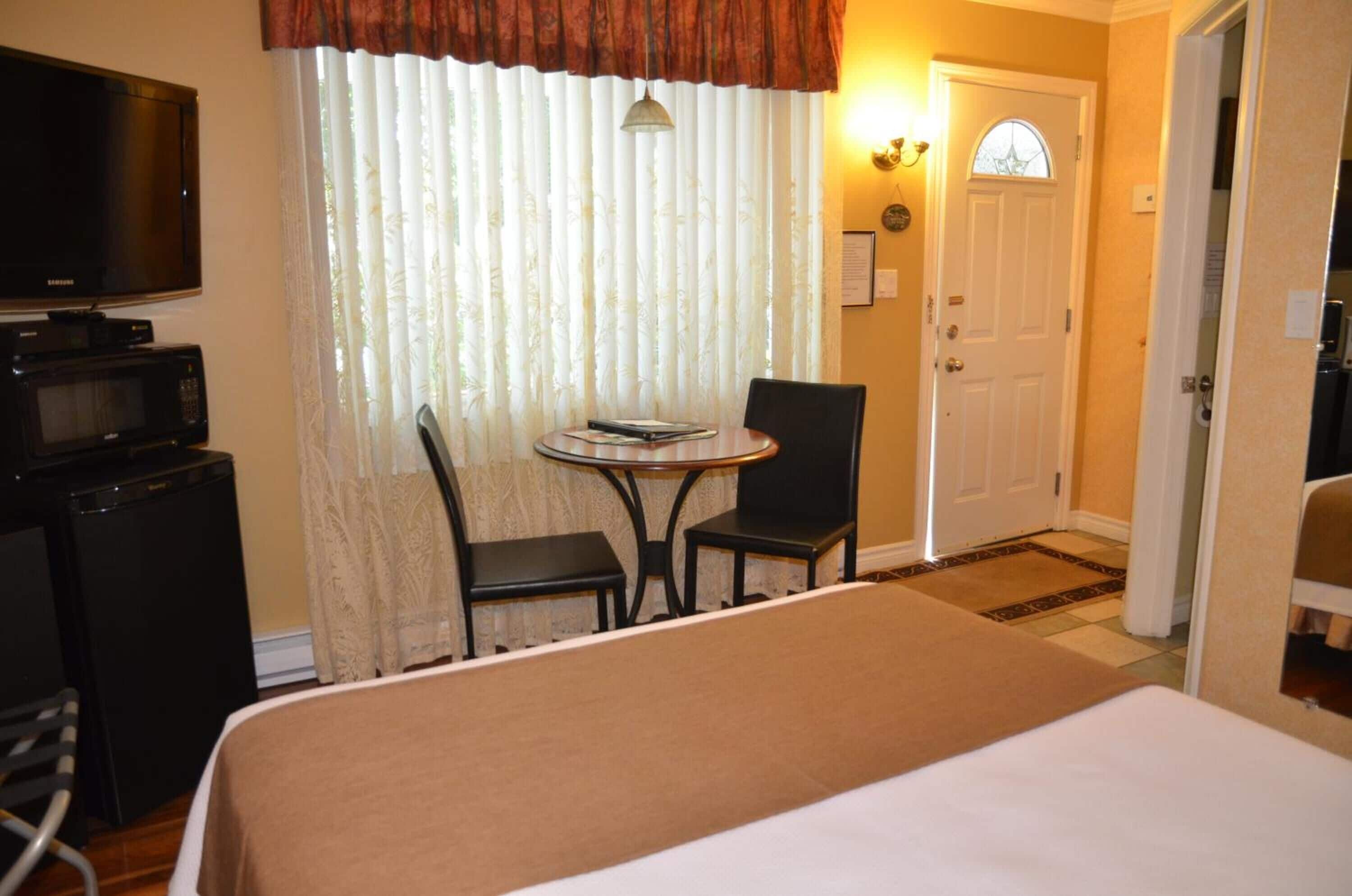 A hotel room with a bed, a TV, a microwave, a small table with chairs, and a door with a window.