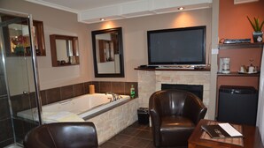 A bathroom with a bathtub, a glass shower enclosure, a mirror, and a television mounted above a fireplace. - Motel Derfal (Repentigny)