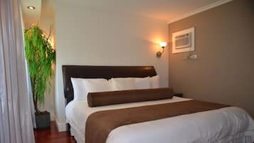 Una cama bien hecha con ropa de cama blanca y marrón, una planta en maceta y un aire acondicionado de pared.
