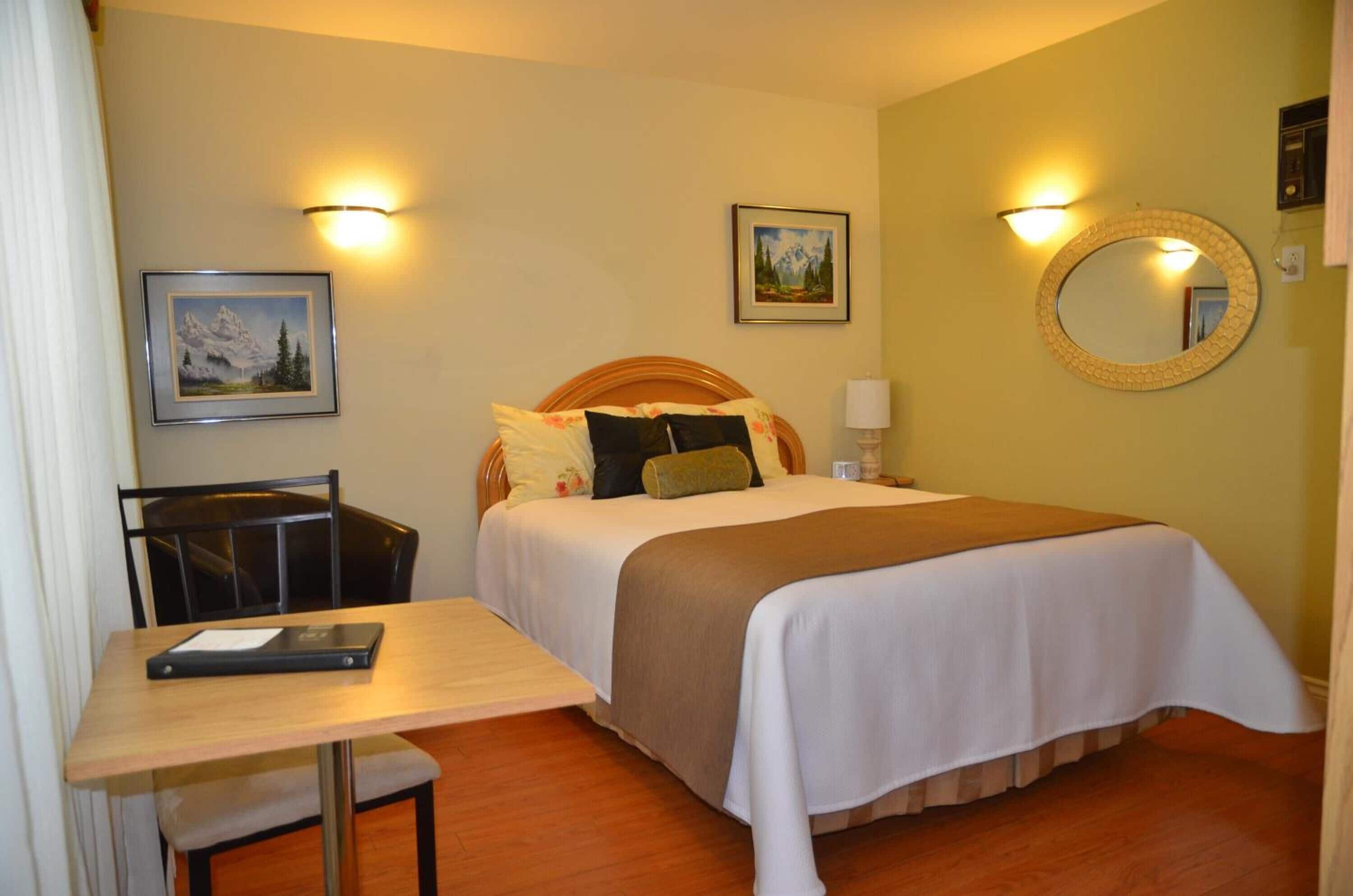 A hotel room with a bed, a desk, a chair, a mirror, and two wall-mounted lights.