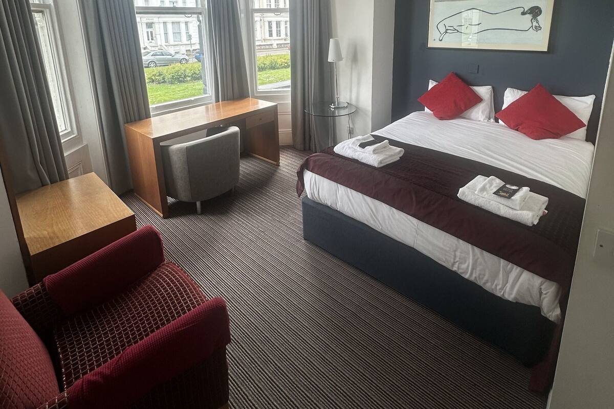 A hotel room with a bed, a desk, a chair, and a large window.