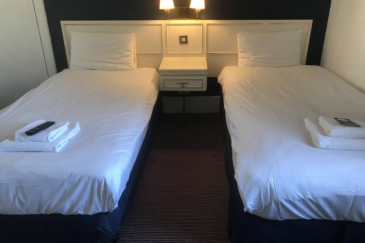 A hotel room with two beds, white linens, a dark carpet, and two bedside lamps.