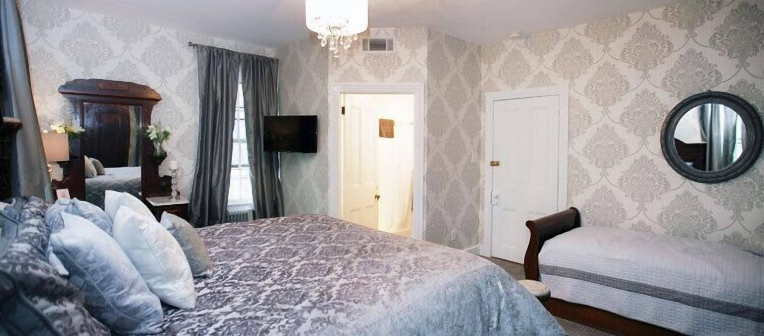 A bedroom with a large bed, a chair, a television, and a door leading to another room.