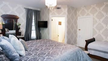 A bedroom with a large bed, a chair, a television, and a door leading to another room.