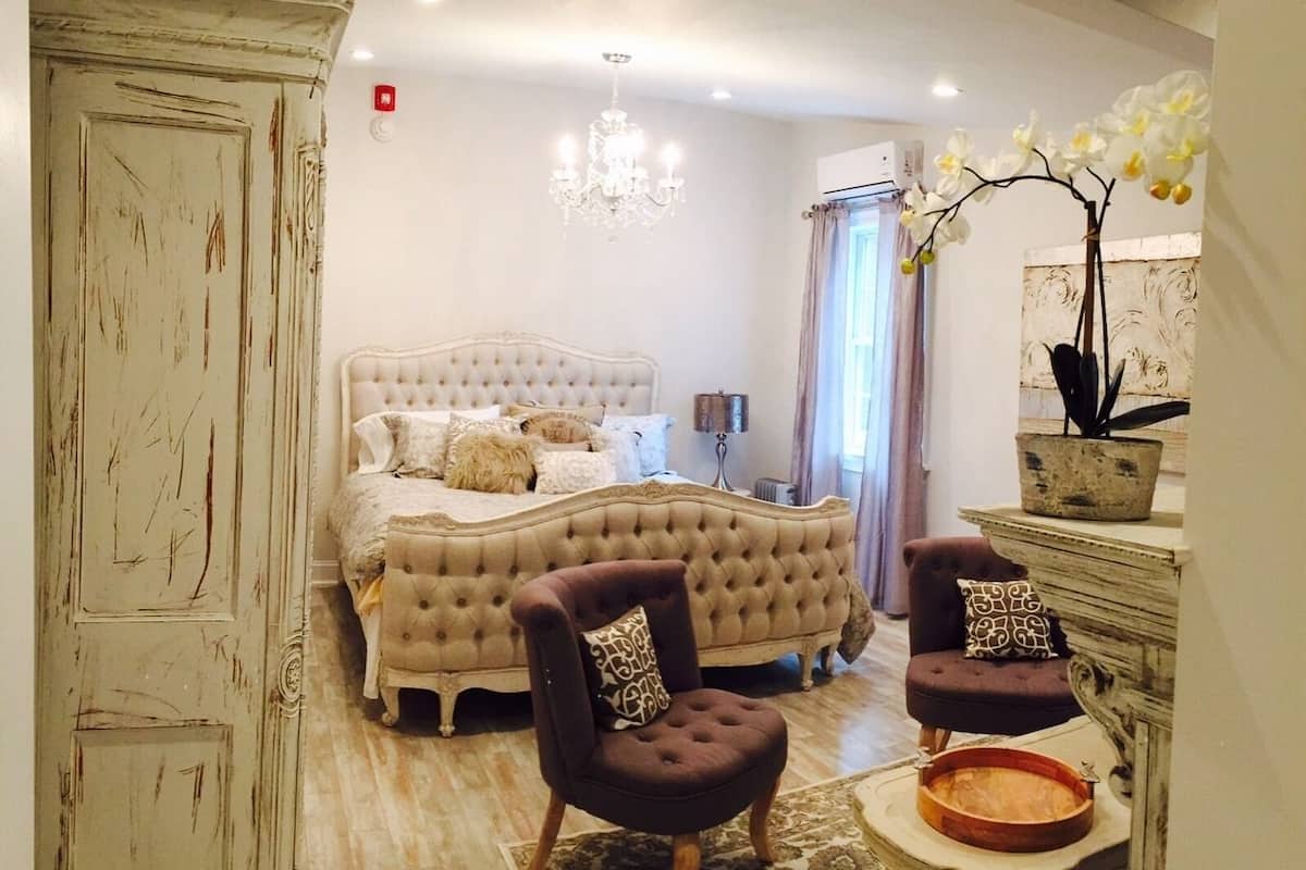 A bedroom with a large bed, two armchairs, a dresser, and a chandelier.