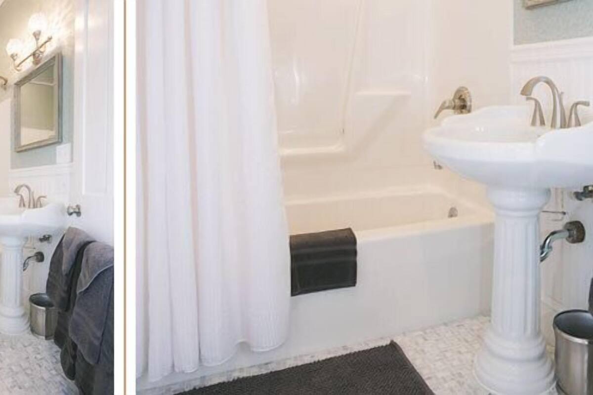 A bathroom with a pedestal sink, a bathtub, and a mirror.