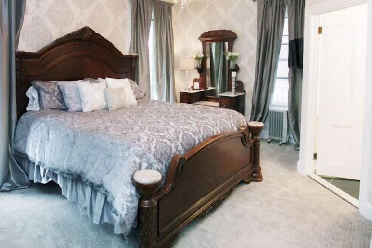 A bedroom with a large bed, a wooden headboard, a nightstand, a mirror, and a dresser.