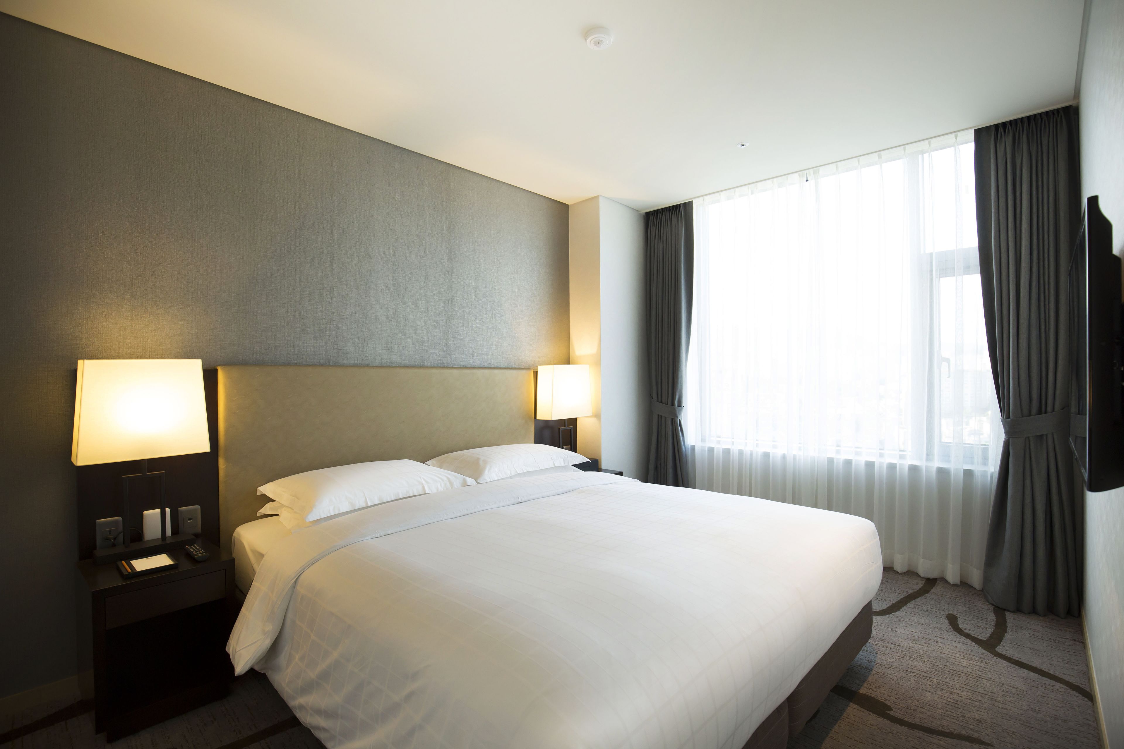 A hotel room with a large bed, two bedside lamps, a flat-screen TV, and a window with curtains.