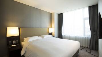 A hotel room with a large bed, two bedside lamps, a flat-screen TV, and a window with curtains.