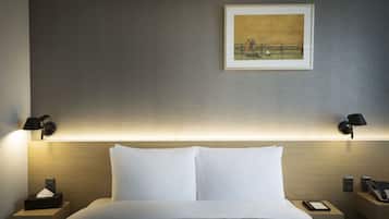 A neatly made bed with white linens, two bedside tables with lamps, a framed painting on the wall, and a bedside phone.