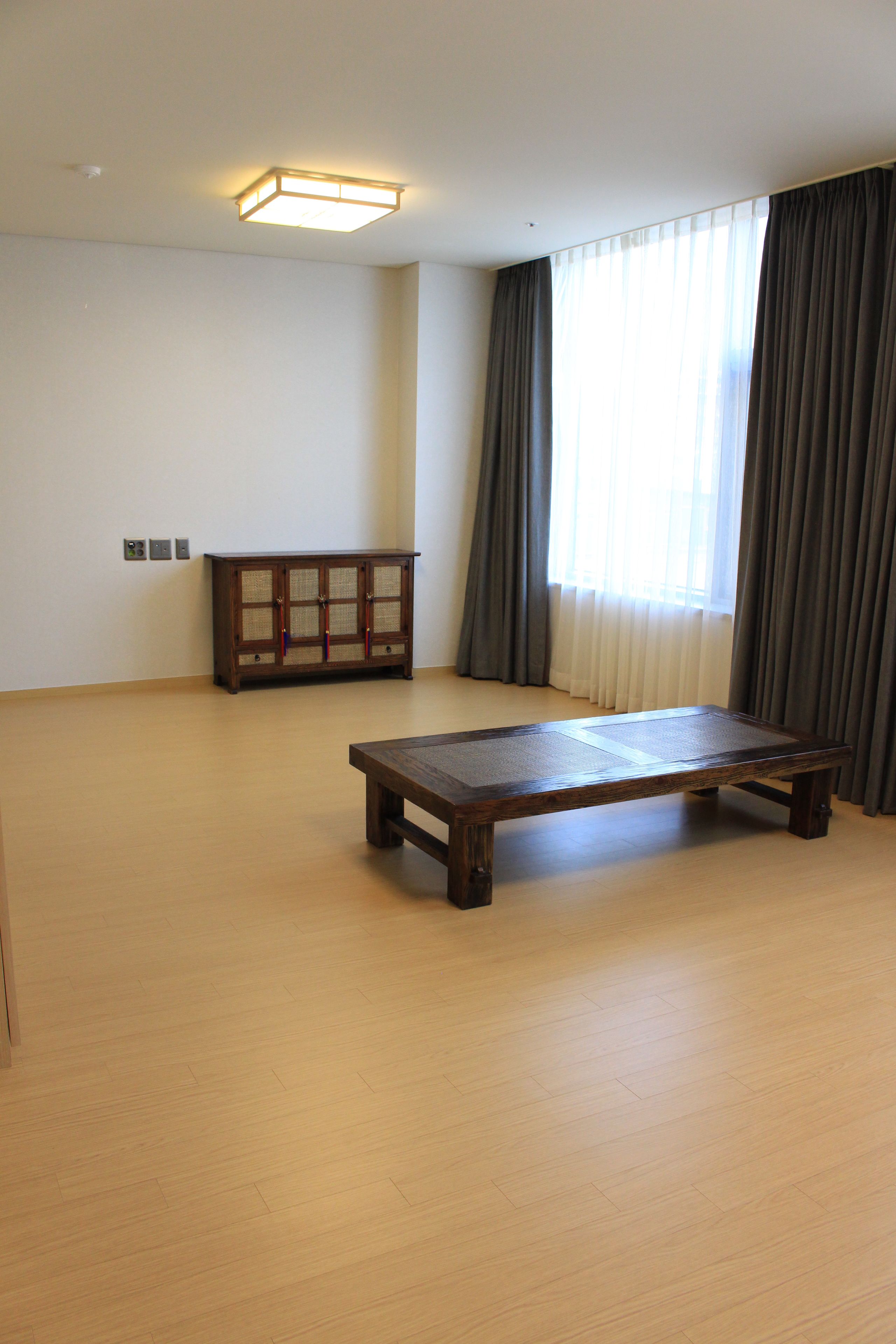 Una habitación amplia con una mesa de madera, un armario y un ventanal con cortinas.