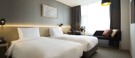 Habitación de hotel con dos camas, un escritorio, una silla y un ventanal con cortinas.