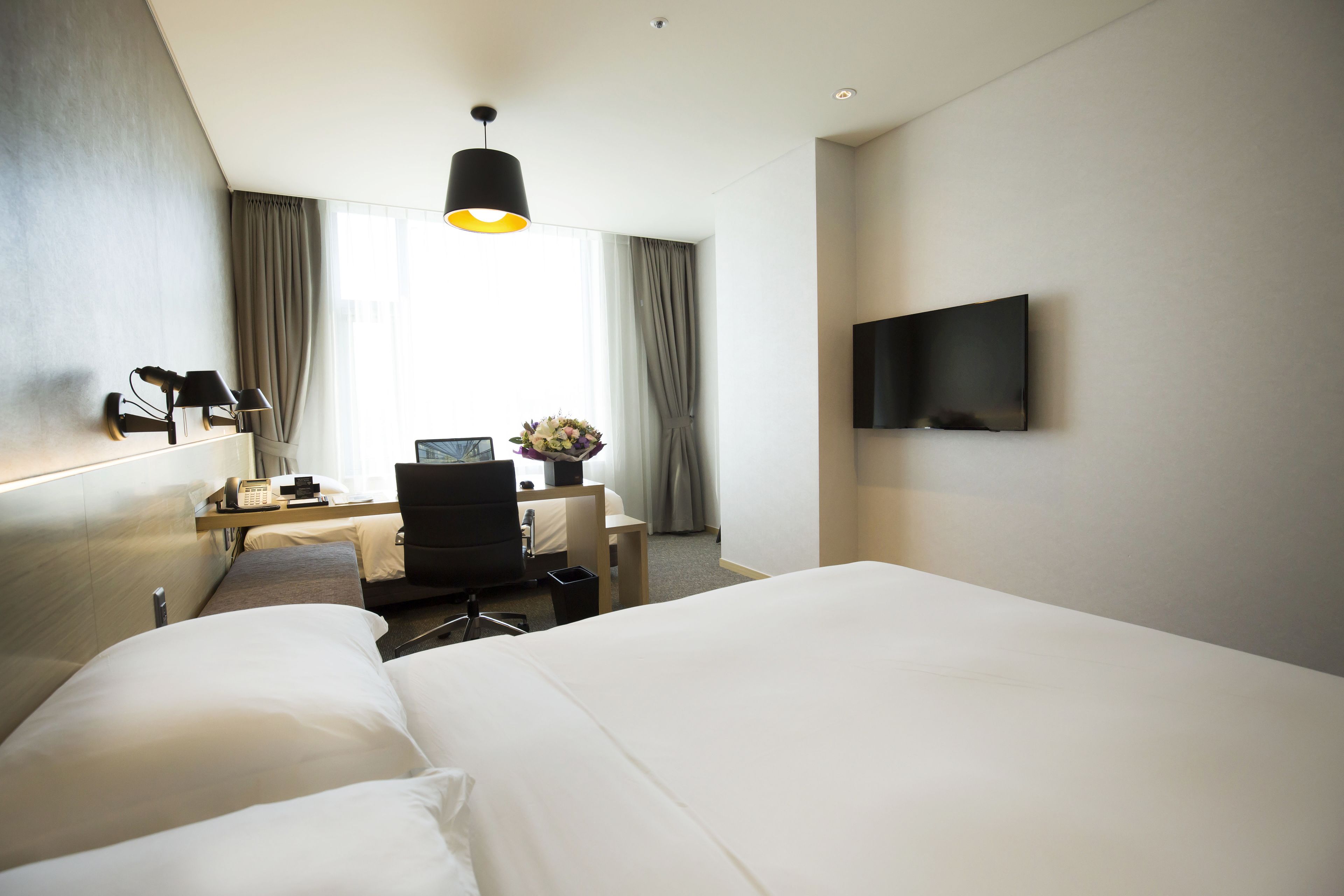 Habitación de hotel con una cama grande, un escritorio con computadora, una silla, una lámpara y un televisor en la pared.