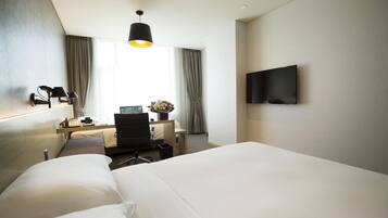 Habitación de hotel con una cama grande, un escritorio con computadora, una silla, una lámpara y un televisor en la pared.