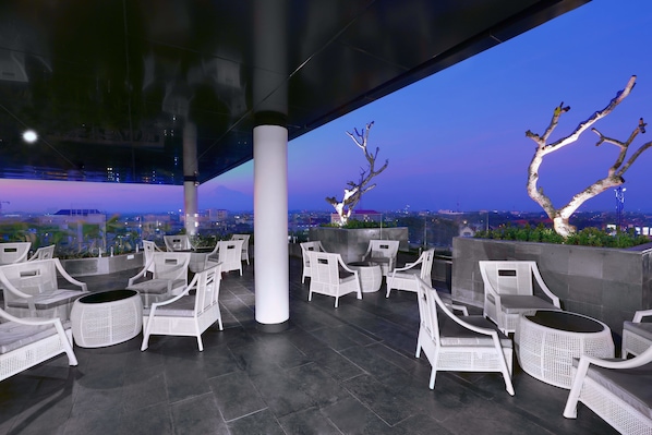 An outdoor seating area with white wicker furniture and a view of the cityscape at dusk.