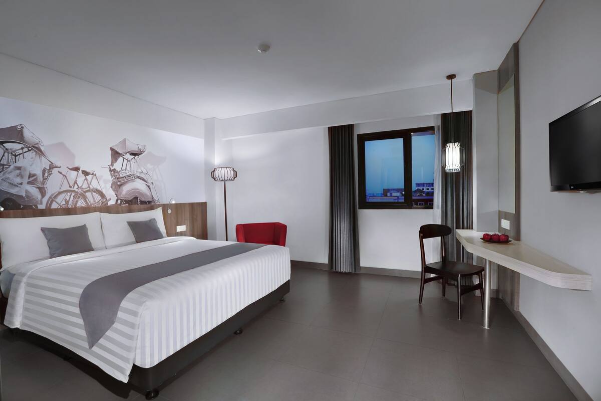 A modern hotel room with a large bed, a desk, a chair, and a TV.