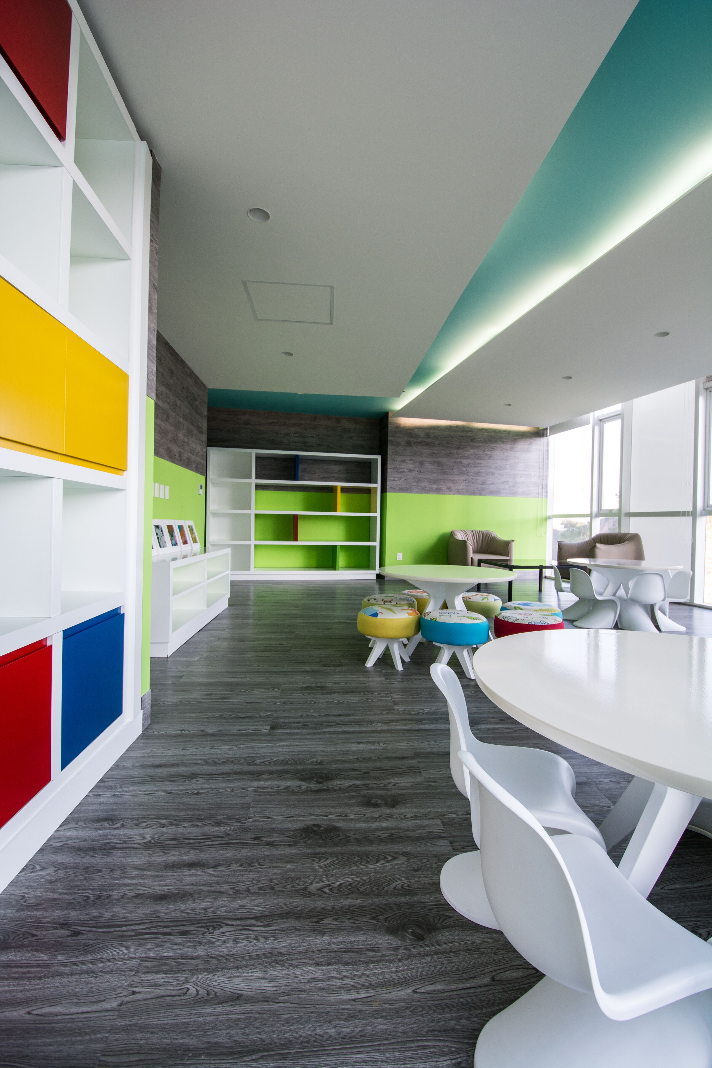 Eine moderne Bibliothek mit weißen Regalen, farbenfrohen Stauraumelementen und einem runden Tisch mit weißen Stühlen.