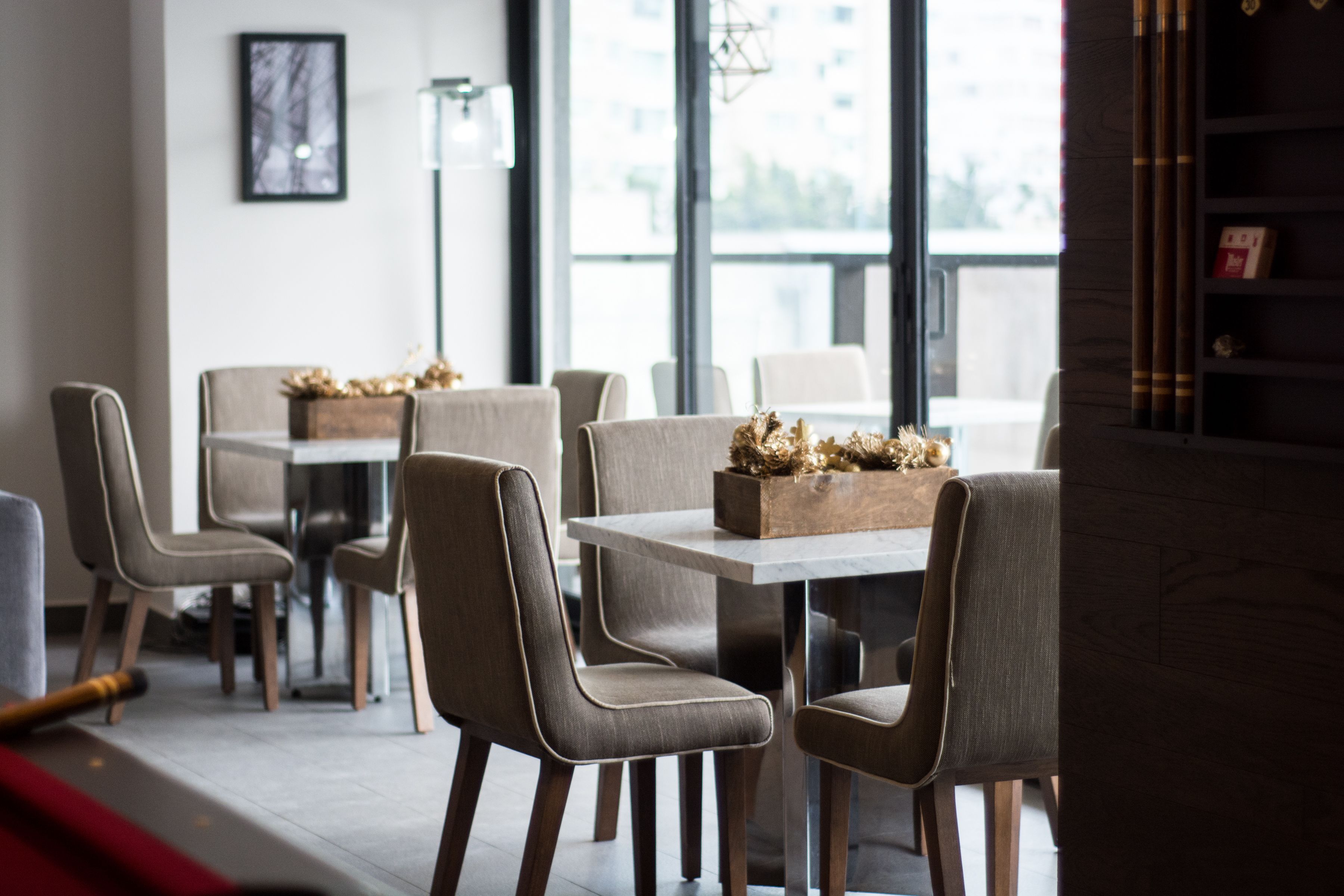 Un comedor moderno con mesas y sillas, un ventanal con vistas y una planta decorativa en el alféizar.