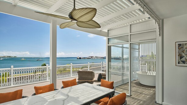 A spacious outdoor area with a table and chairs, a ceiling fan, and a view of the ocean.