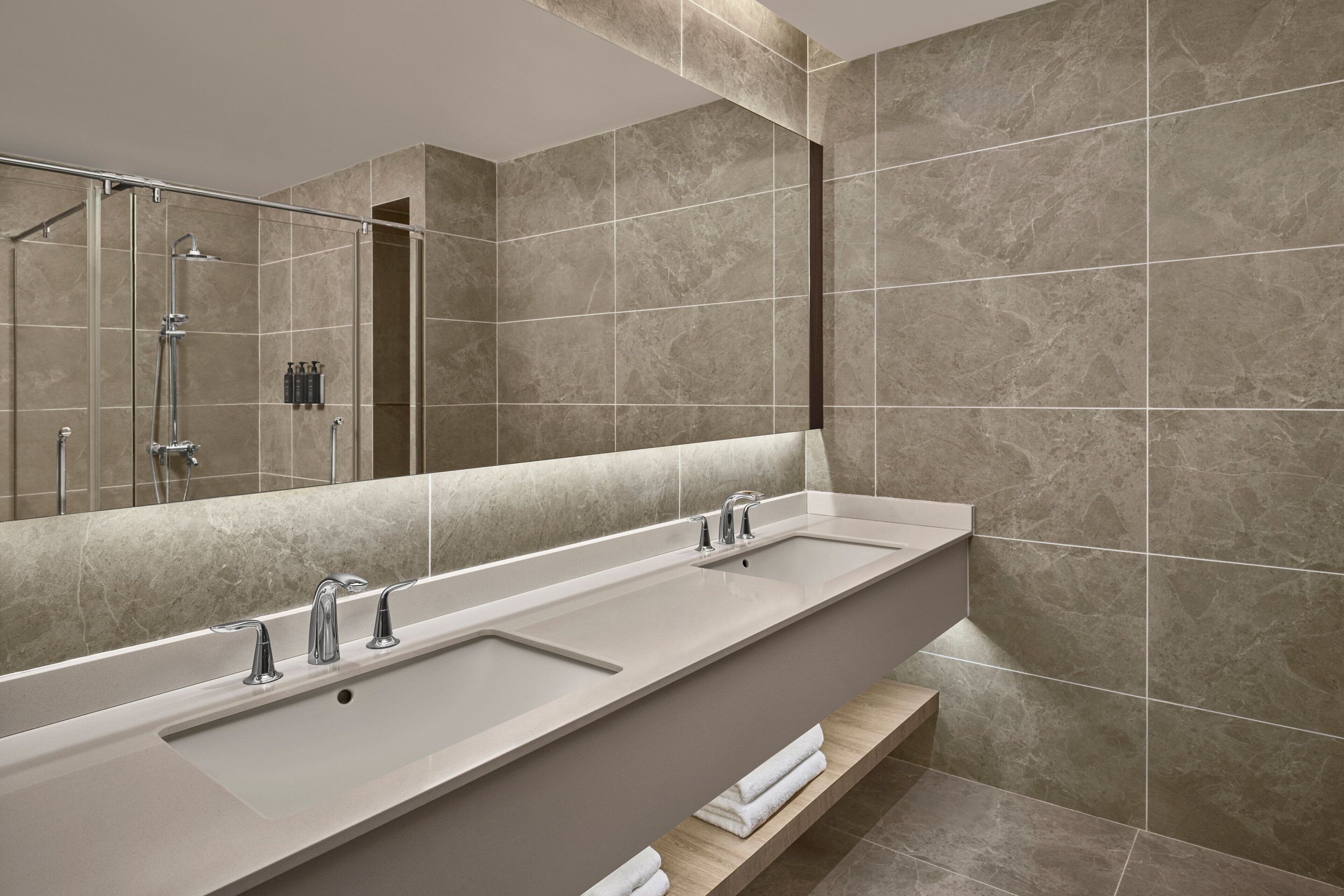 A modern bathroom with a long, rectangular sink, a large mirror, and a shower area.