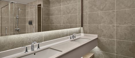 A modern bathroom with a long, rectangular sink, a large mirror, and a shower area.