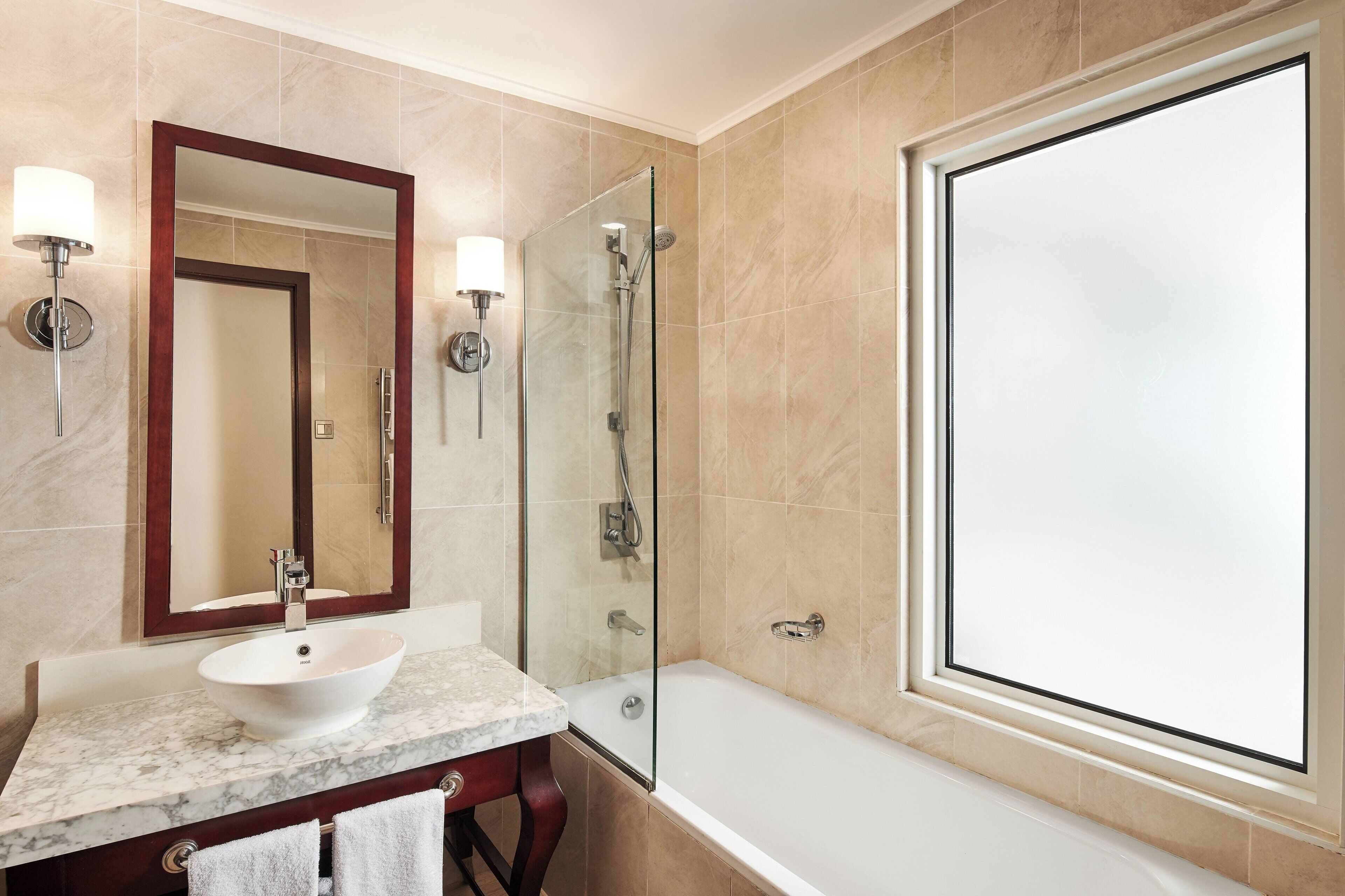 Un baño con lavamanos de mármol, un espejo grande, ducha con mampara de vidrio y una bañera.