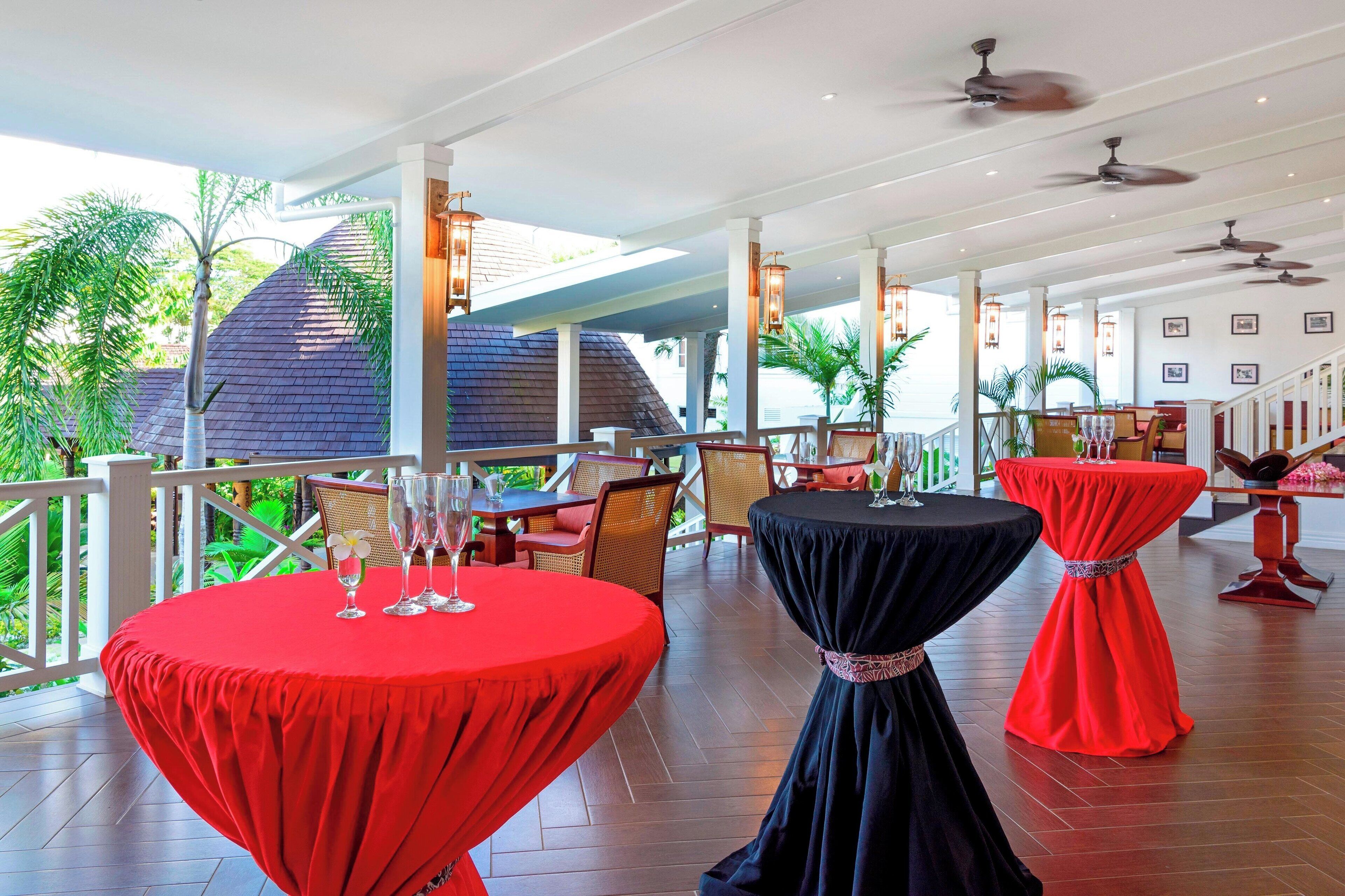 A covered outdoor dining area with round tables, ceiling fans, and a view of the surrounding greenery.