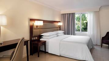 Una habitación de hotel con una cama, un escritorio, una silla y un ventanal con cortinas.