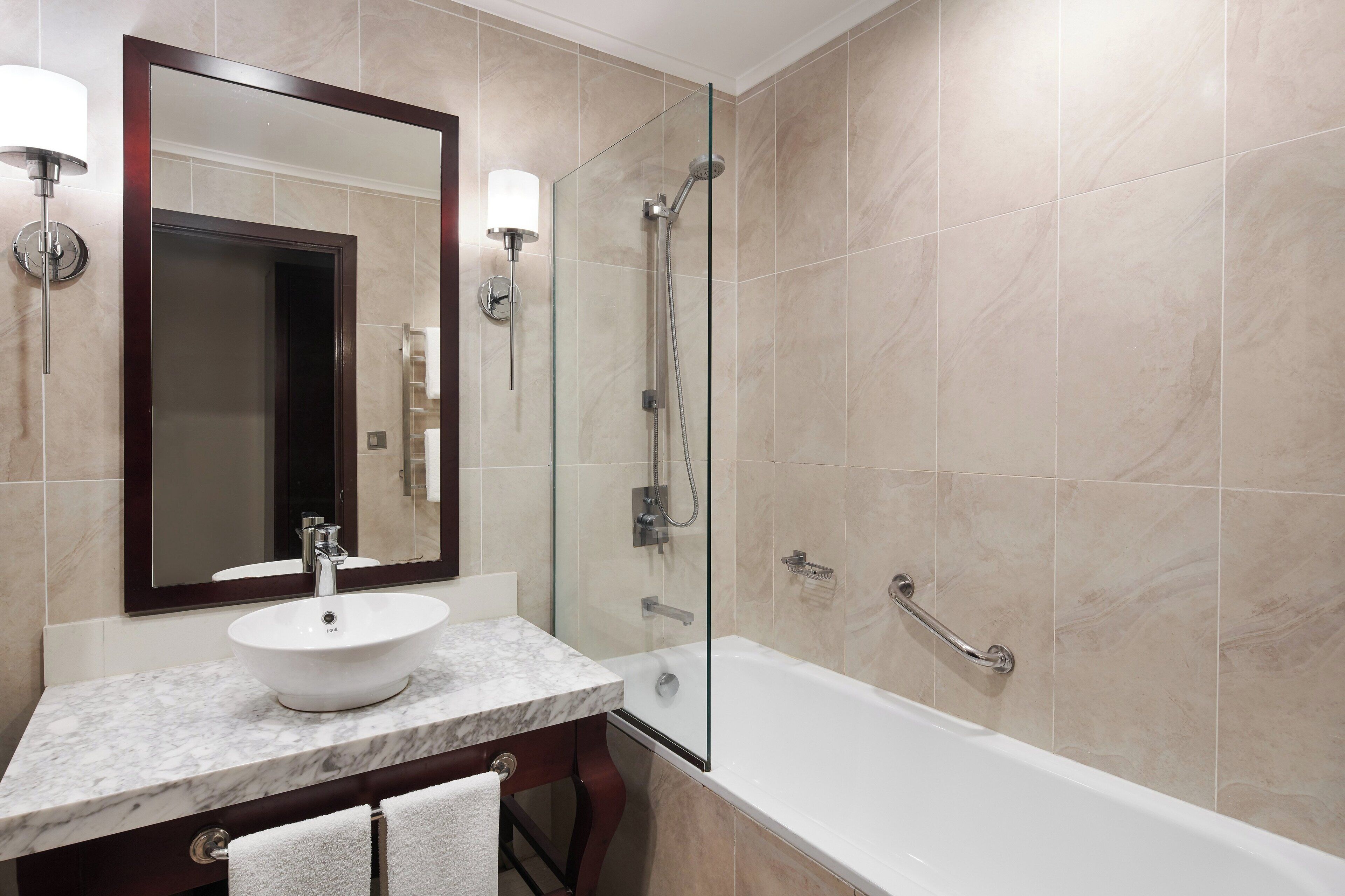 Un baño con lavamanos de mármol, ducha con mampara de vidrio y un espejo grande.