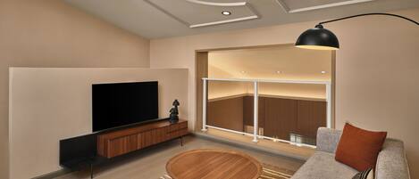 Una sala de estar moderna con un televisor de pantalla plana, una mesa de centro de madera, un sofá gris y un amplio ventanal con vista al interior.
