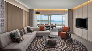 A modern living room with a sofa, coffee table, and a TV. There is a balcony with a view of the sea.