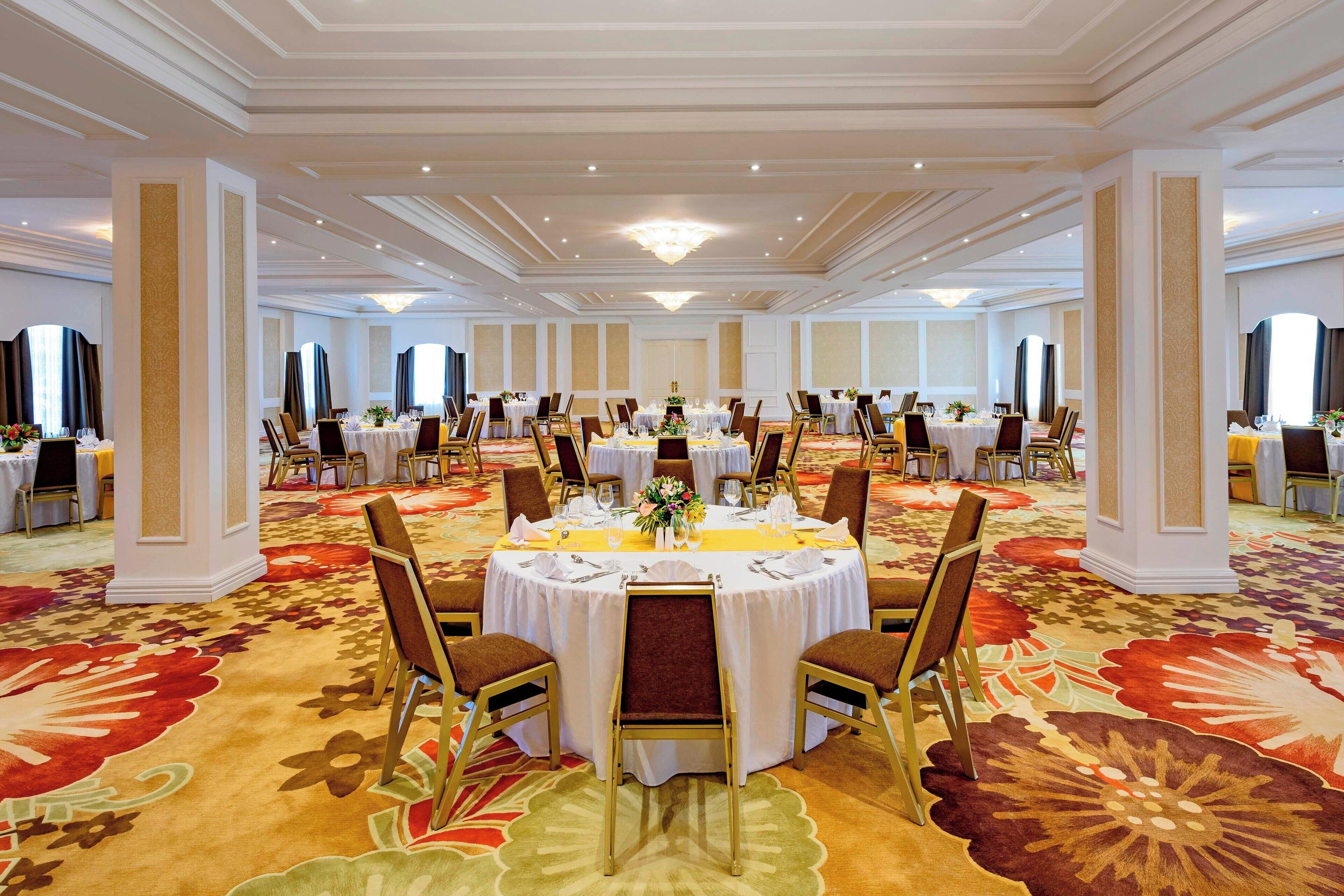 Un amplio salón de banquetes con mesas redondas dispuestas para comer, que cuenta con piso alfombrado y una lámpara de candelabro.