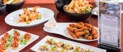 A variety of appetizers on a wooden table, including shrimp, chicken nuggets, and other finger foods.