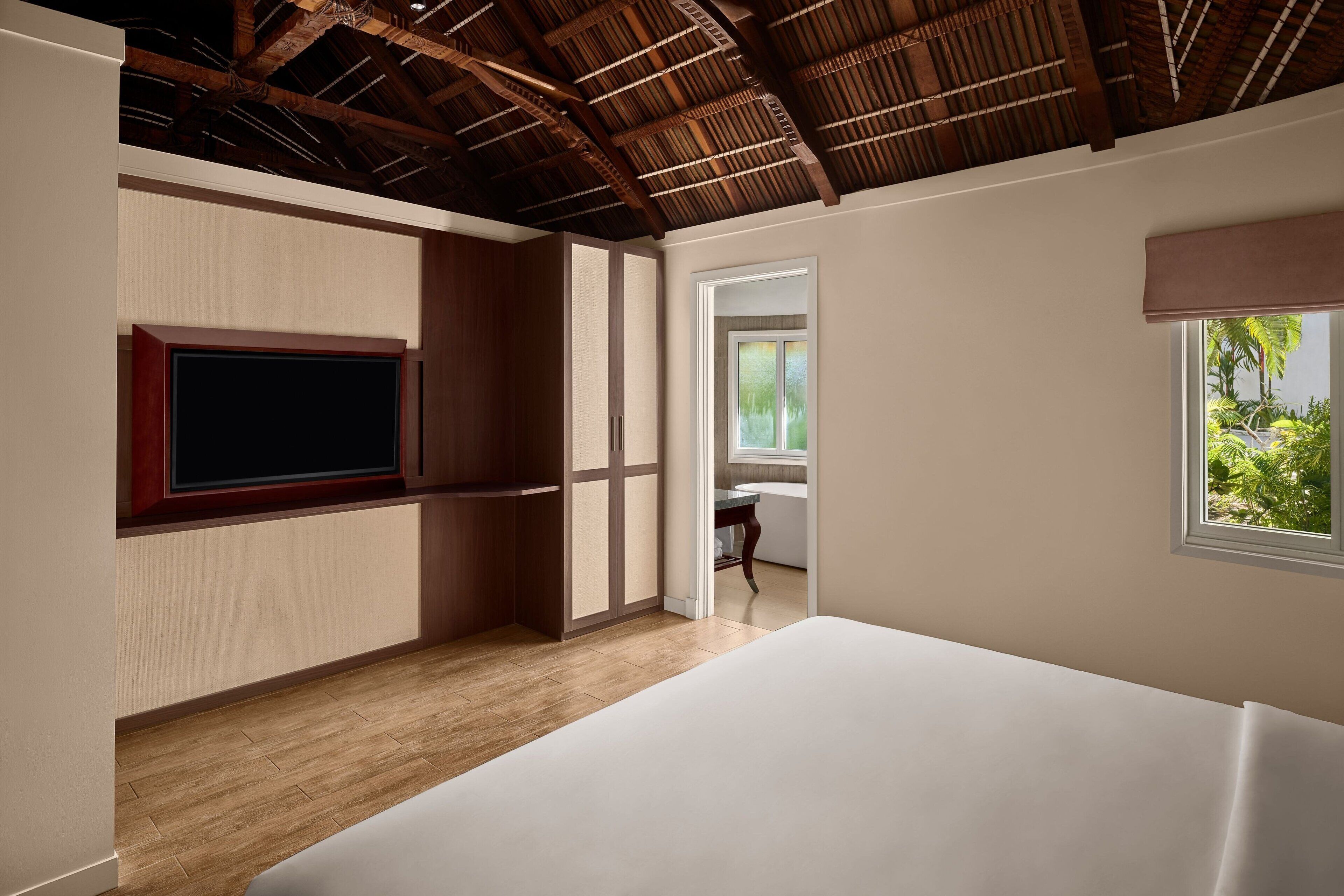 Una camera da letto con soffitto in legno, un letto grande, una TV a muro e una finestra vista sul verde.