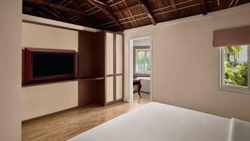 A bedroom with a wooden ceiling, a large bed, a TV mounted on the wall, and a window with a view of greenery.