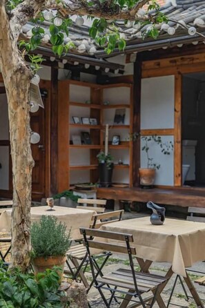 An outdoor seating area with tables and chairs, a wooden pergola, and a potted plant.