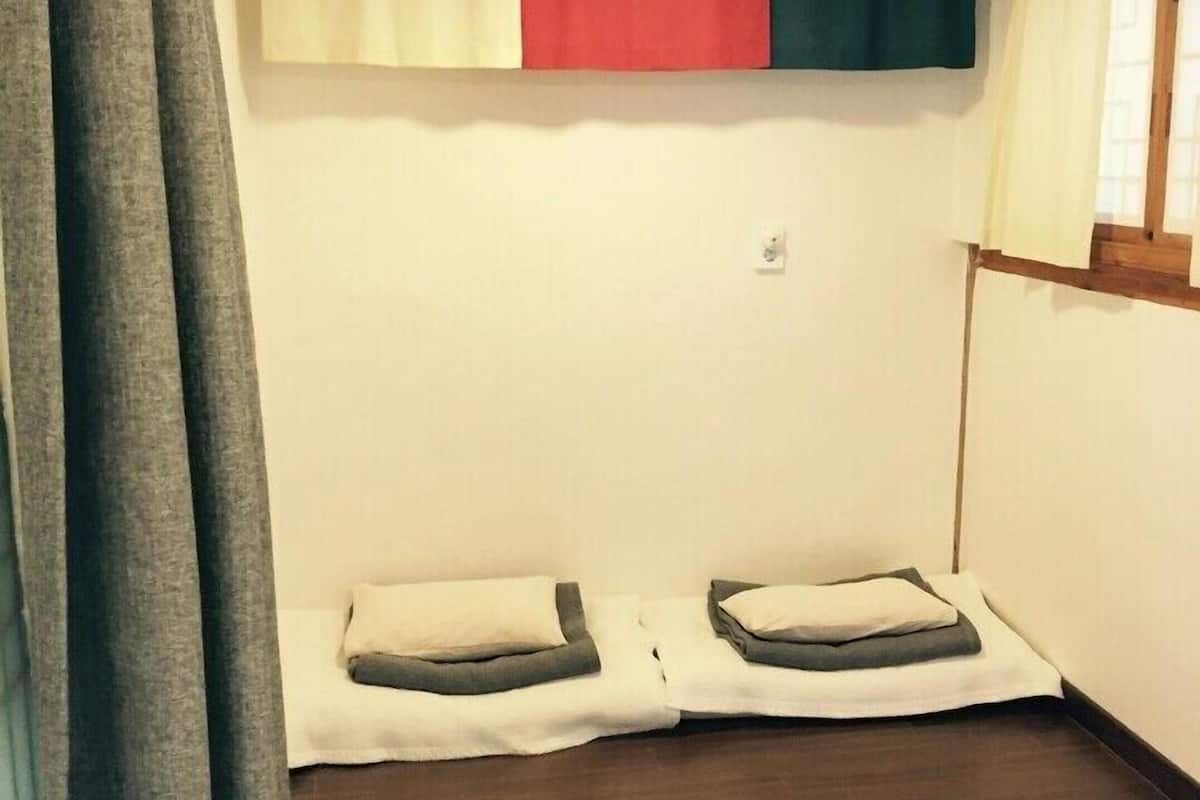 A small, simple room with a bed, a window, and a ceiling light.