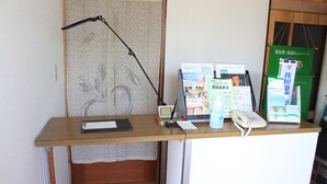 Una mesa de recepción con una lámpara, un teléfono, un expositor para folletos y una pequeña alfombra roja.