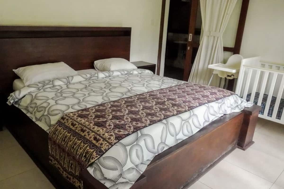A bedroom with a large bed, a wooden headboard, a white crib, and a white chair.