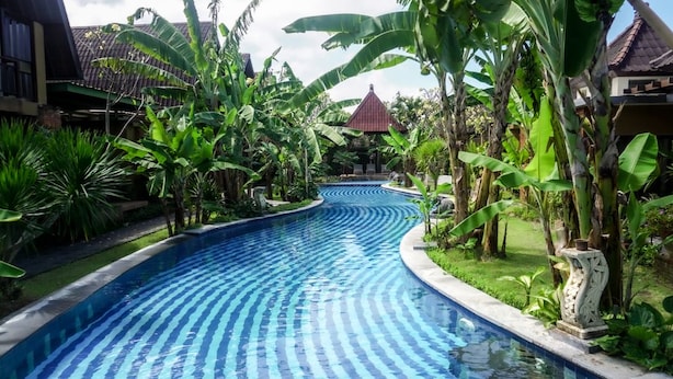 Uma piscina com design curvo, rodeada por vegetação exuberante e plantas tropicais.