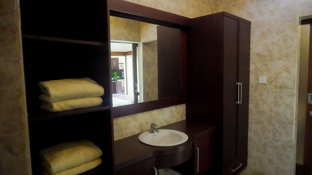 A bathroom with a dark wood vanity, a white sink, and a mirror above it. There are two shelves with folded towels.