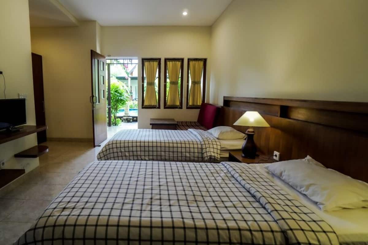 A hotel room with two beds, a TV, a bedside table, a lamp, and a view of the outside.