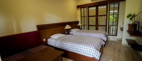 Quarto de hotel com duas camas, um banco de madeira, uma escrivaninha e uma TV em uma estante.