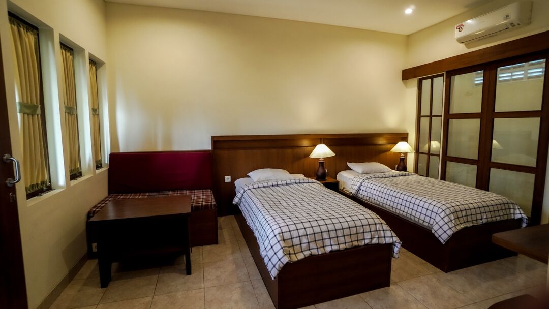 A hotel room with two beds, a sofa, a small table, and a window with curtains.