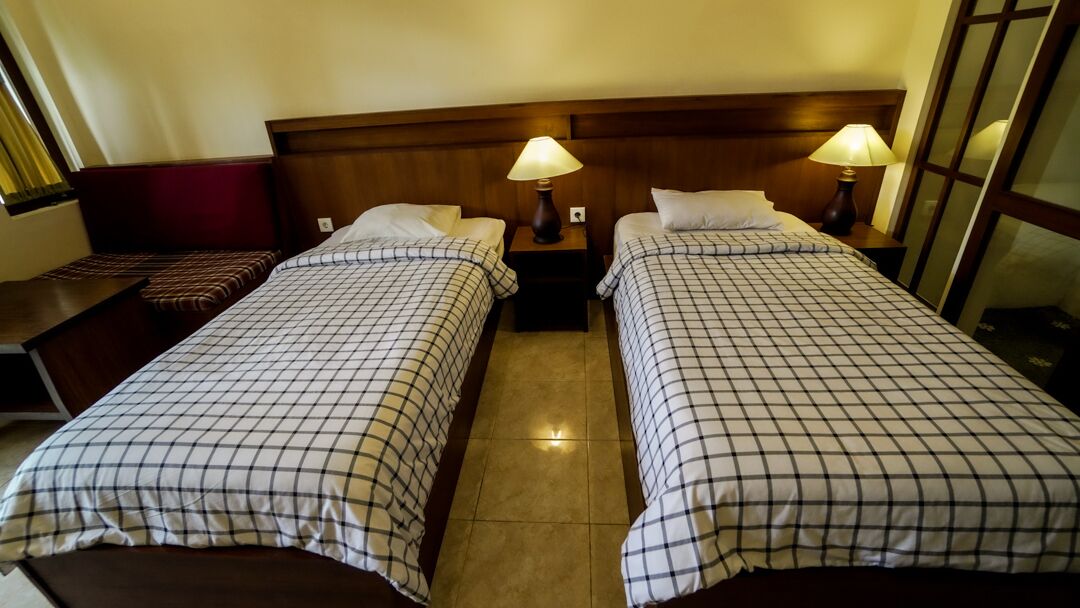 Habitación de hotel con dos camas, cada una con cabecero y mesitas de noche con lámparas.