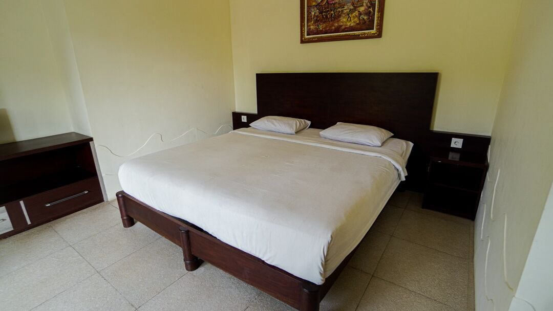 A bedroom with a large bed, wooden headboard, two bedside tables, and a wall-mounted painting.