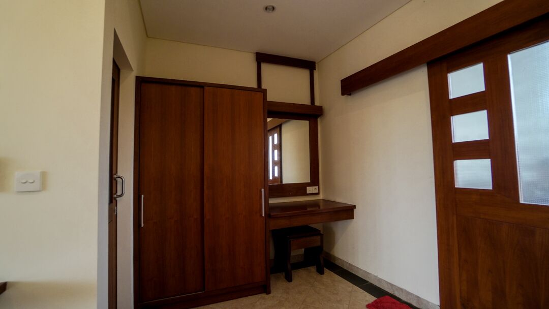 A room with a wooden wardrobe, a small desk, and a mirror.