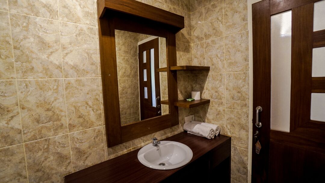 Un baño con pared de mármol, tocador de madera con lavamanos, espejo y toallero.