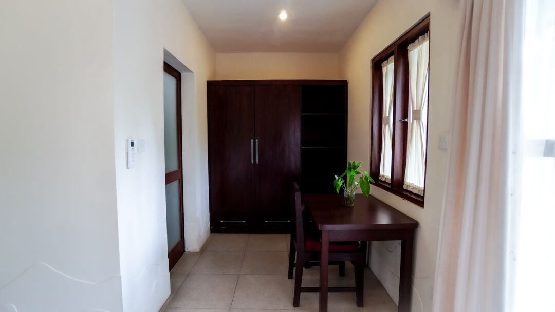 A room with a wooden table and chairs, a dark wooden wardrobe, and a window with curtains.
